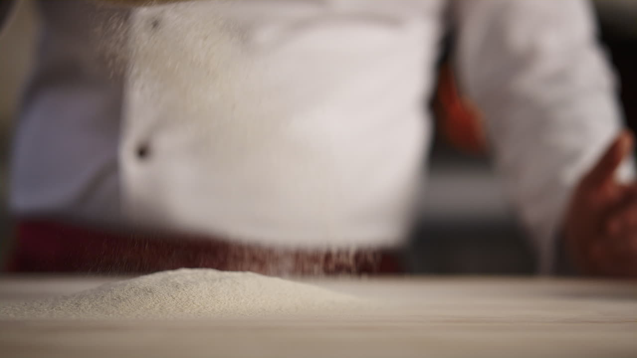 Professional chef cooking flour on cafe kitchen. Man baker sifting using sieve.
