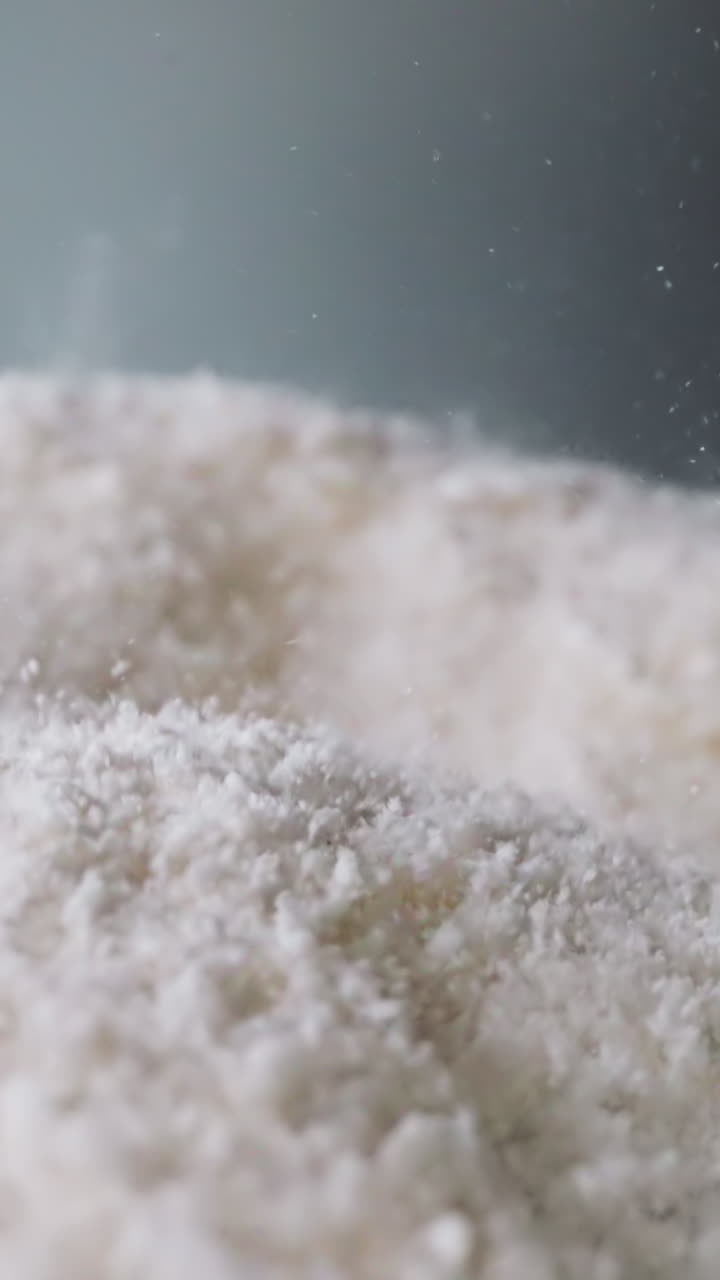 Coke powder bounces on concave surface against dark grey wall. White substance with psychoactive properties sifting through sieve moves lying on working panel macro