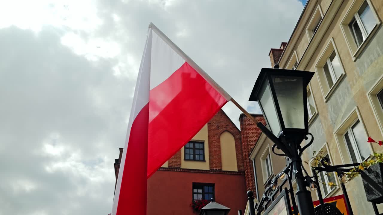 Slow motion shot of Polish flag waving peacefully under cloudy sky in city