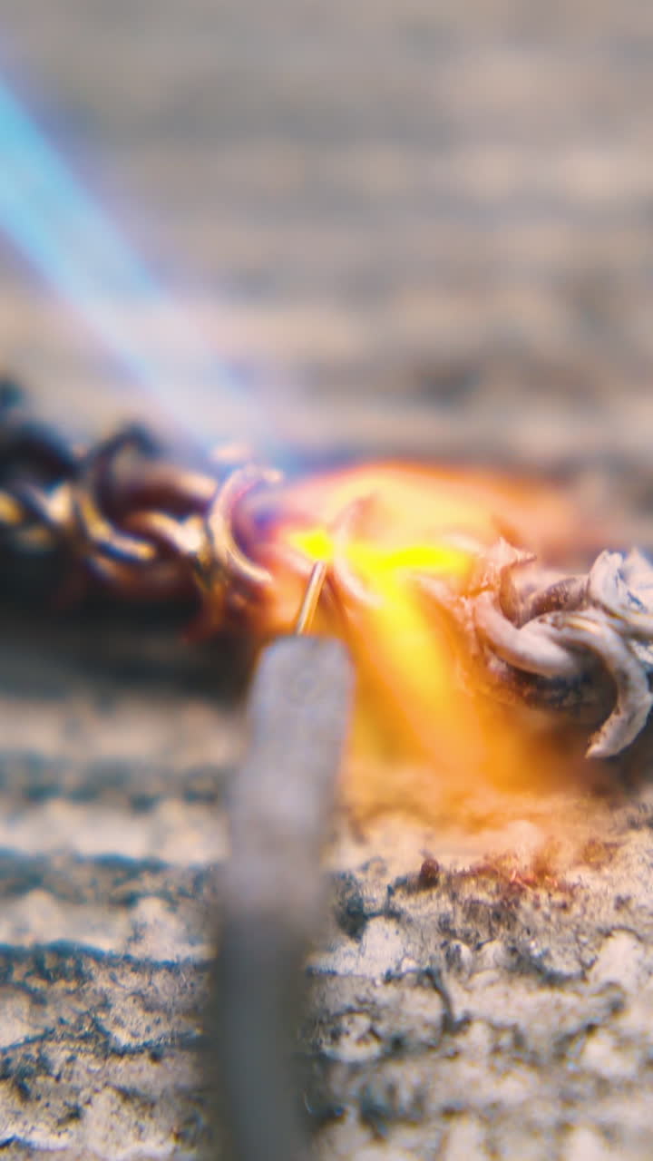 CU shot: professional goldsmith welds long gold chain with heating gas burner and special tool on fireproof sheet closeup