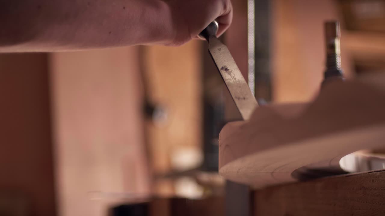 Un abile artigiano usa uno scalpello metallico affilato per modellare un pezzo di legno curvo in un'officina. La ripresa al rallentatore evidenzia la precisione della lavorazione manuale del legno
