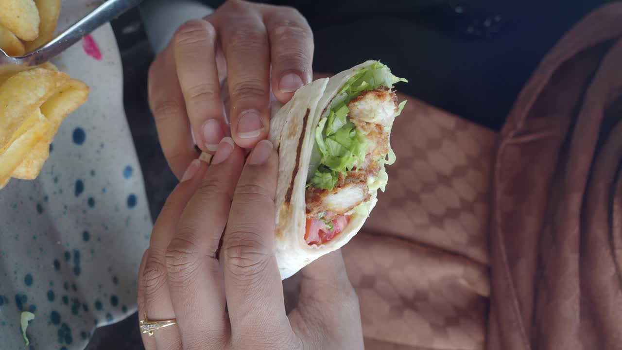 Person eating a chicken wrap with fries