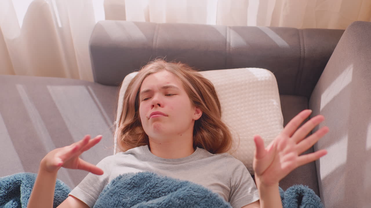 Top down view of remote worker dancing gently on couch covered in blanket during morning time, eyes closed enjoying peaceful atmosphere as sunlight shines through curtains