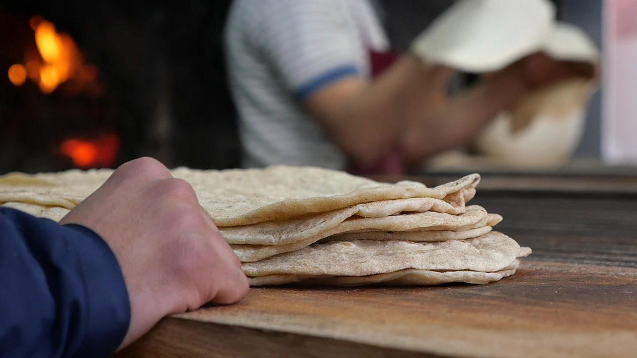 Stack of Fresh Flatbreads with Baker Working by Wood-Fired Oven