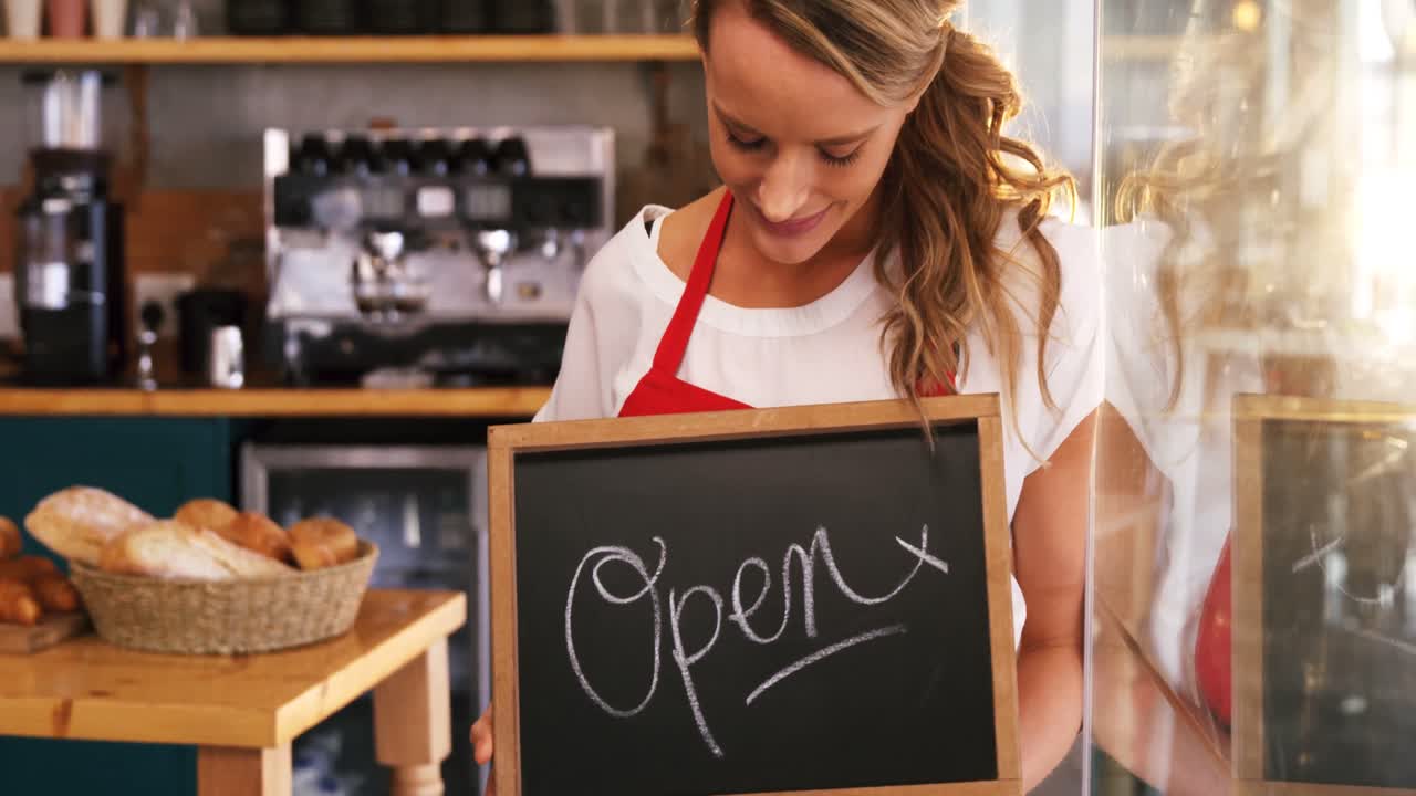 Cameriera sorridente che regge un cartello con scritto "aperto"