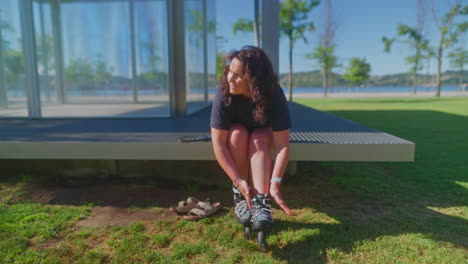 woman putting on rollerblades in a park by a river