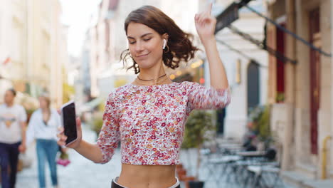 Happy-woman-in-wireless-earphones-dancing,-listening-music-in-smartphone-dancing-walking-city-street