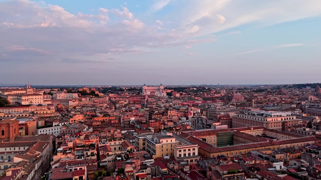 La calda luce serale inonda i fitti tetti storici di Roma mentre un drone sorvola la città verso un orizzonte lontano