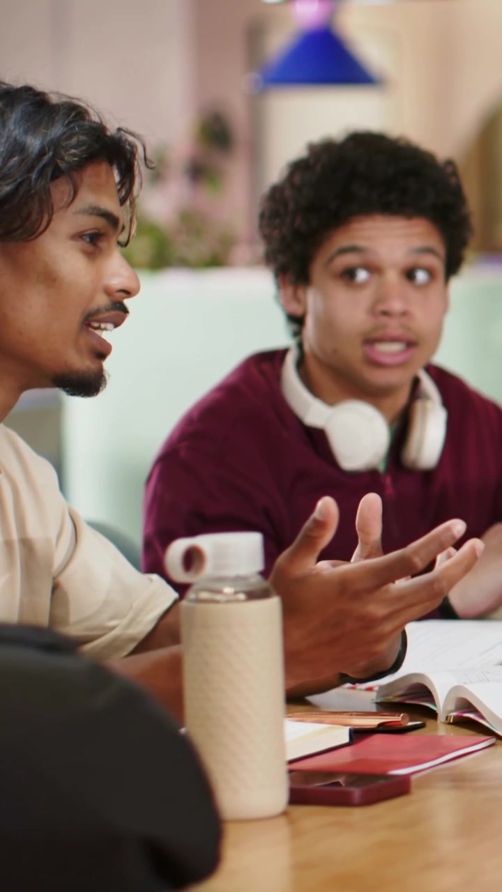 Vertical video: Starting left man in beige tee explaining while right man following notes, studying