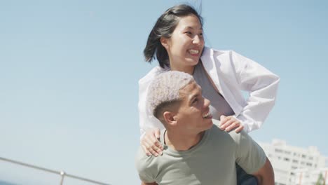 happy biracial couple walking together and embracing on promenade, in slow motion