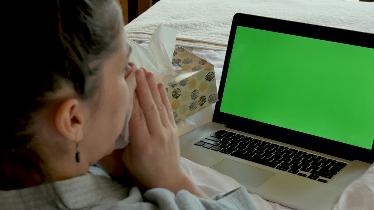 mujer soplando la nariz con una computadora de pantalla verde asintiendo con la cabeza sí