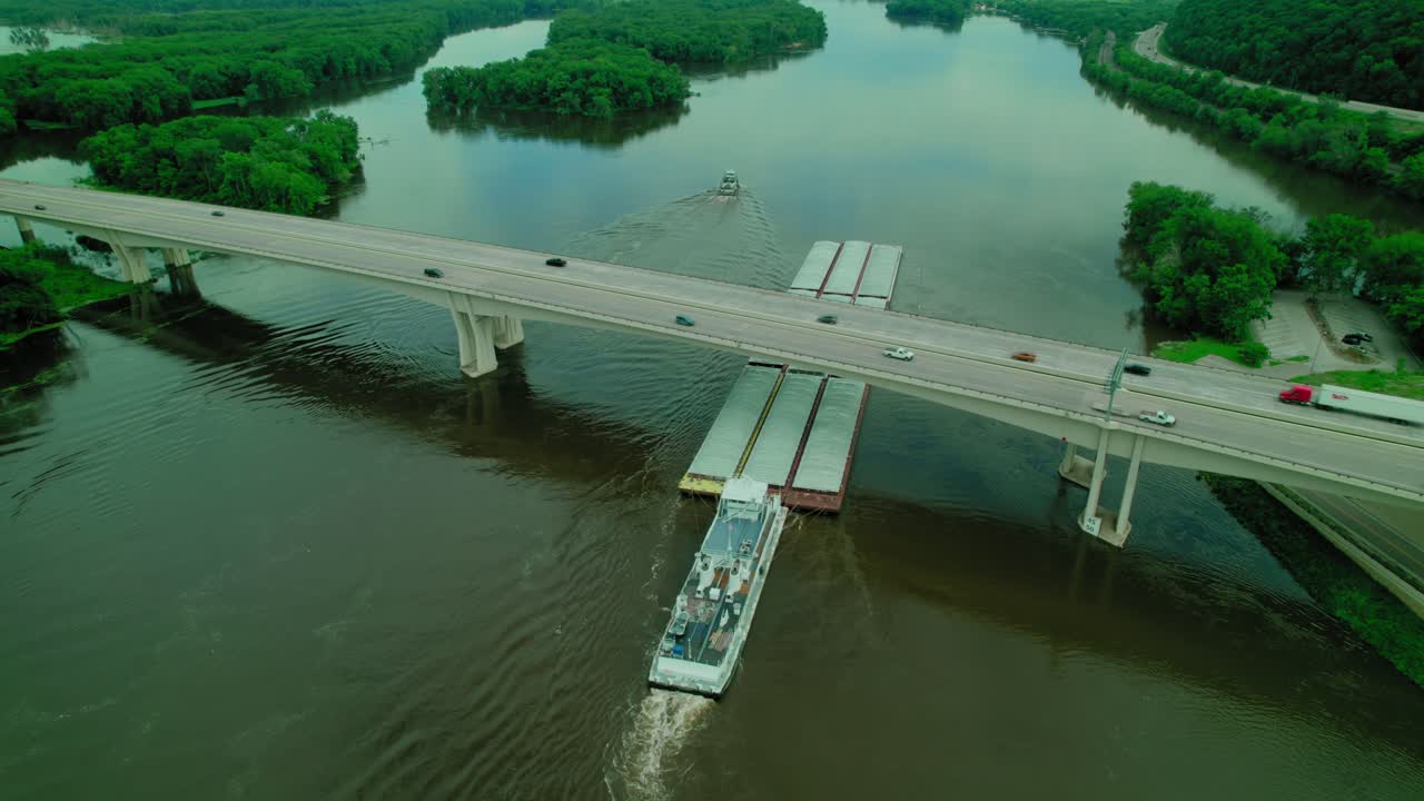 Aerial of tugboat pushing barge, scow, floating platform on missisipi river in wisconsin under Dresbach Bridge