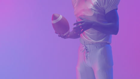 video de la sección media de un jugador de fútbol americano afroamericano con pelota sobre fondo púrpura
