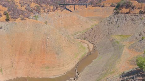 Erstaunliche-Luftaufnahme-über-Dem-Von-Dürre-Betroffenen-Kalifornischen-See-Oroville-Mit-Niedrigem-Wasserstand,-Zurückweichender-Küstenlinie-Und-Verbrannten-Bäumen-Und-Wäldern