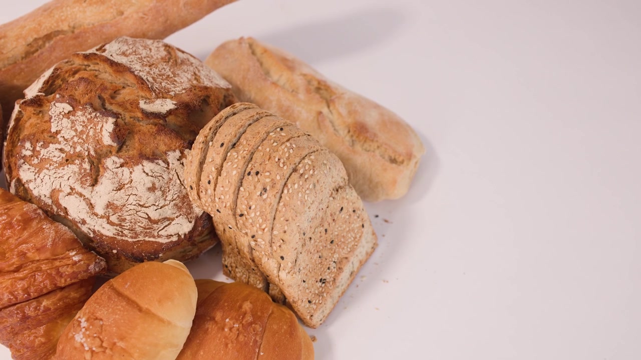 Lenta rotazione di pane a lievitazione naturale, baguette, croissant e pane ai cereali a fette sotto una luminosa illuminazione da studio