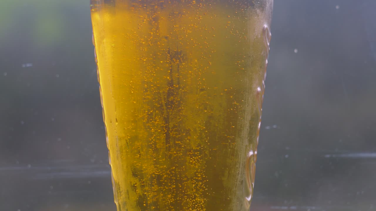 Pan Up Shot of Fresh Cool Lager Beer in Pint Glass with Bubbles Rising in Slow Motion Ready to Enjoy on Hot Summer Day with Glass Background. Alcohol Beverage 4K.