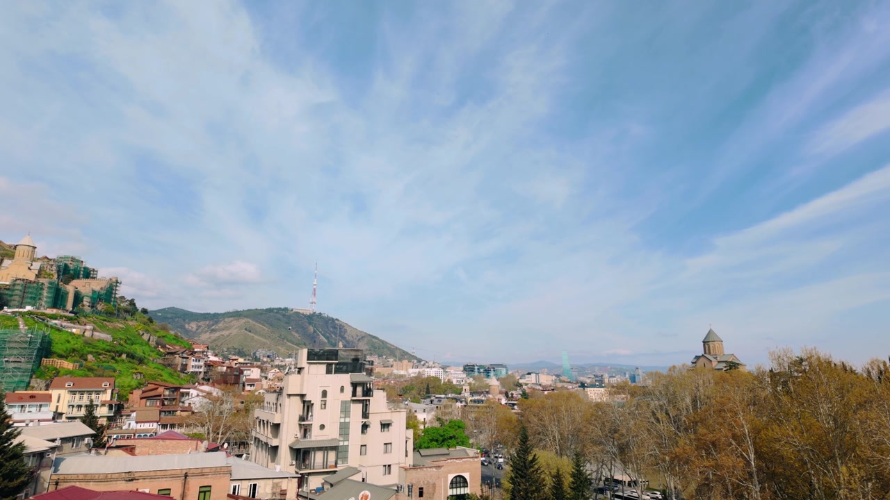 Široký denní pohled na město Tbilisi v Gruzii, nabízející pohled na pevnost Narikala a televizní věž, obklopené směsicí historických a moderních obytných budov a svěžími zelenými plochami.