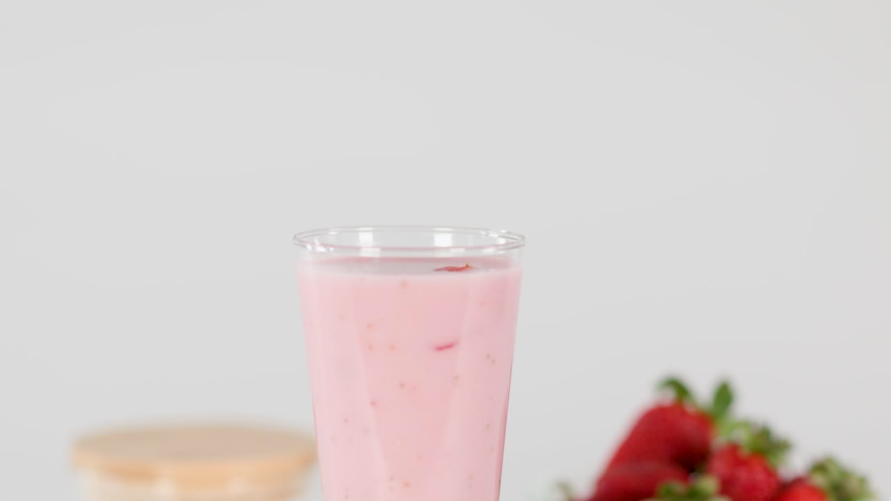 Pink strawberry milkshake with fun straw, fresh strawberries, and flowers on bright, clean background