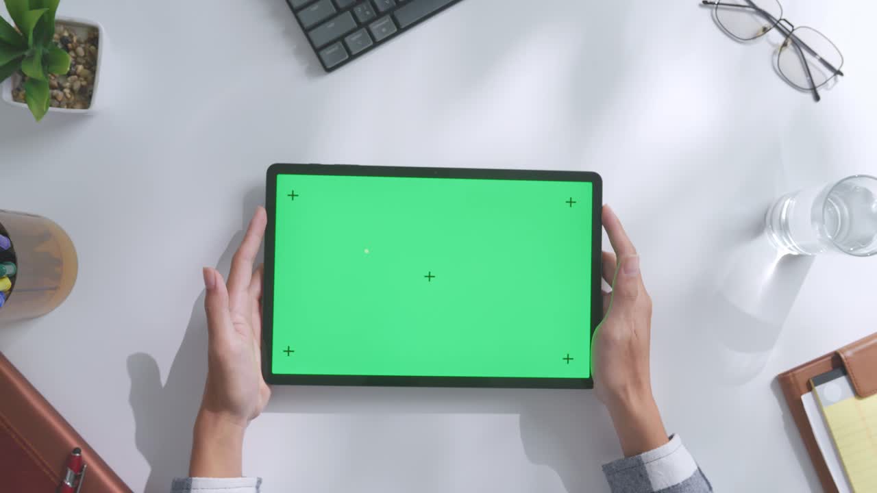 vista de arriba hacia abajo de una computadora portátil con pantalla verde simulada pantalla chromakey en un escritorio de oficina de madera al lado de la libreta con bolígrafos, gafas y un vaso de agua.