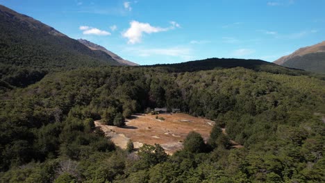 Beautifully-located-tourist-hut-in-forest,-aerial-pull-back,-Greenstone-track,-New-Zealand