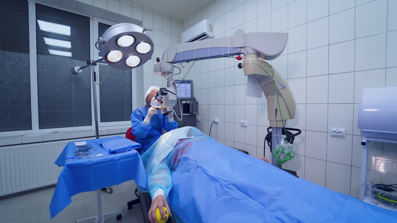 Surgeon performs the operation in latex gloves and mask with microscope. Doctor in medical uniform works with microscope to treat patient's eyes in the light room.