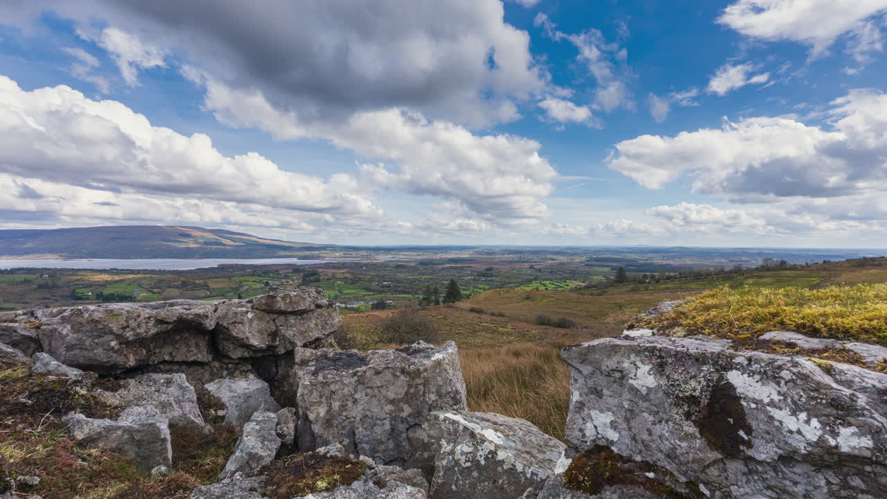 Time lapse of rural landscape with foreground of rocks and grass on hillside and lake in the distance on a spring sunny cloudy day in Arigna mountains in county Leitrim in Ireland
