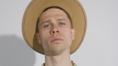 close up portrait of young man with big hat posing and touching his face while looking at camera