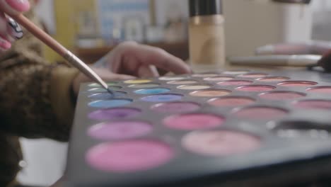 una toma detallada y cercana que captura la hábil aplicación de maquillaje por una niña usando una paleta de maquillaje y un pequeño pincel