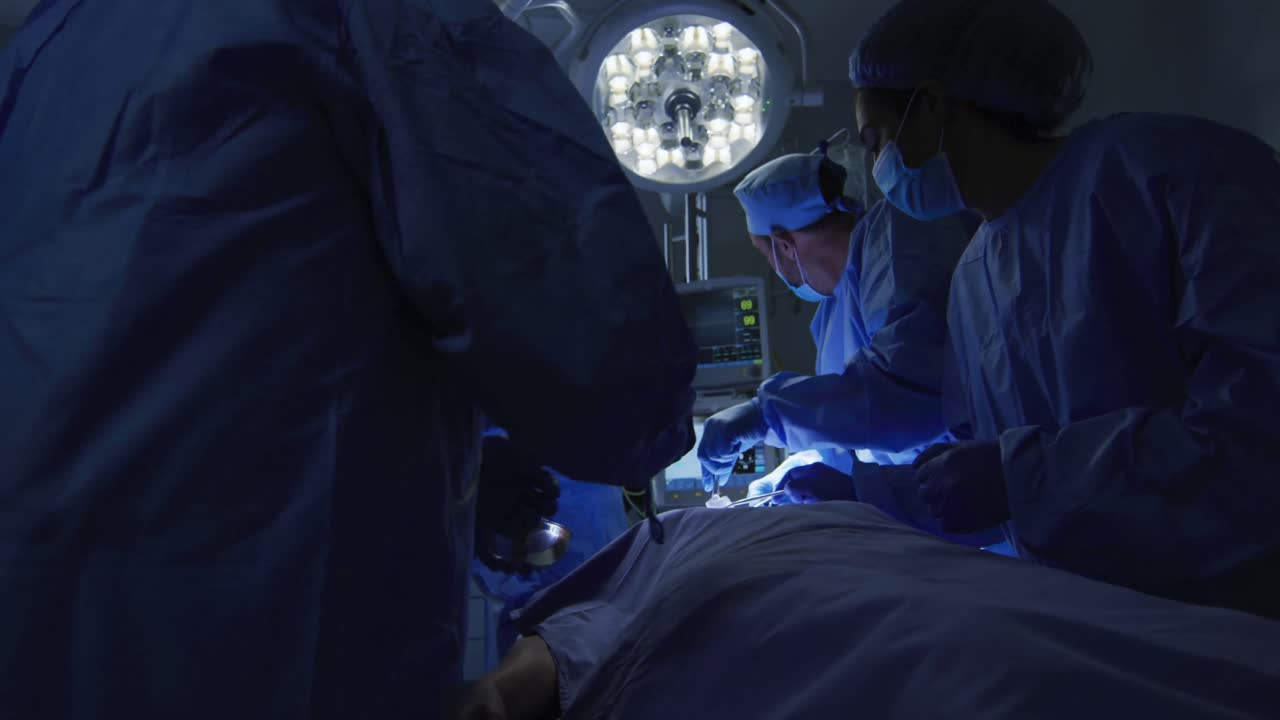 cirujanos de raza mixta con ropa de protección que realizan cirugías en el quirófano