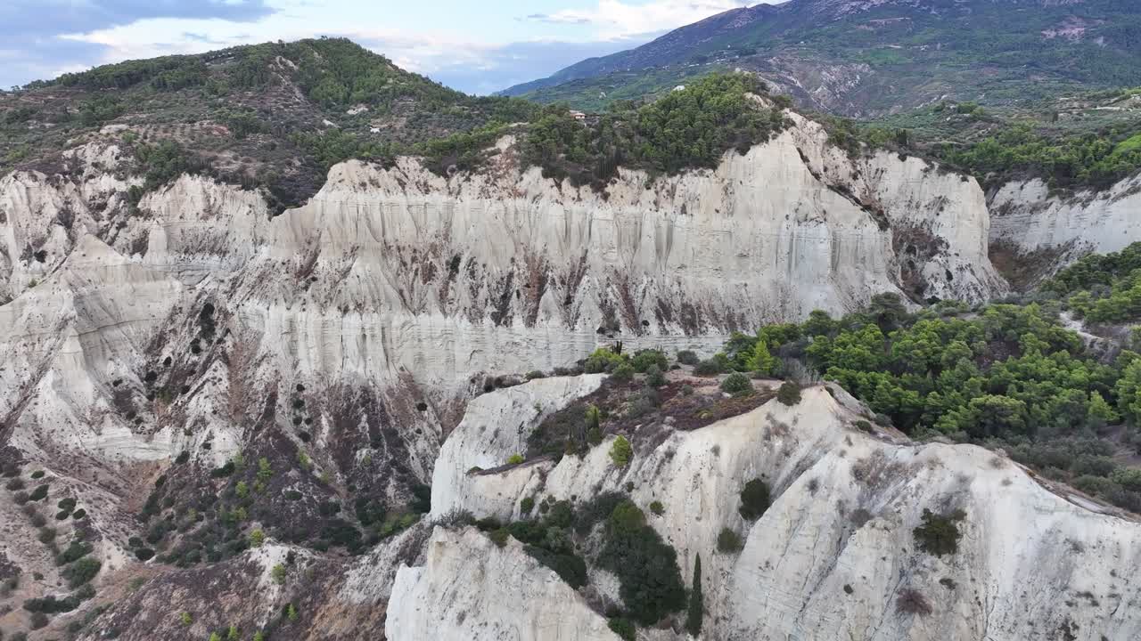Dramatic Greek landscape off the coast of Corinth, showing steep stark white cliffs and lush greenery with storm clouds AERIAL TRUCKING LEFT PAN RIGHT