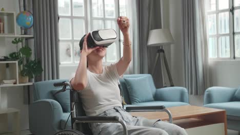 mujer asiática graciosa sentada en una silla de ruedas mientras usa gafas de realidad virtual en casa