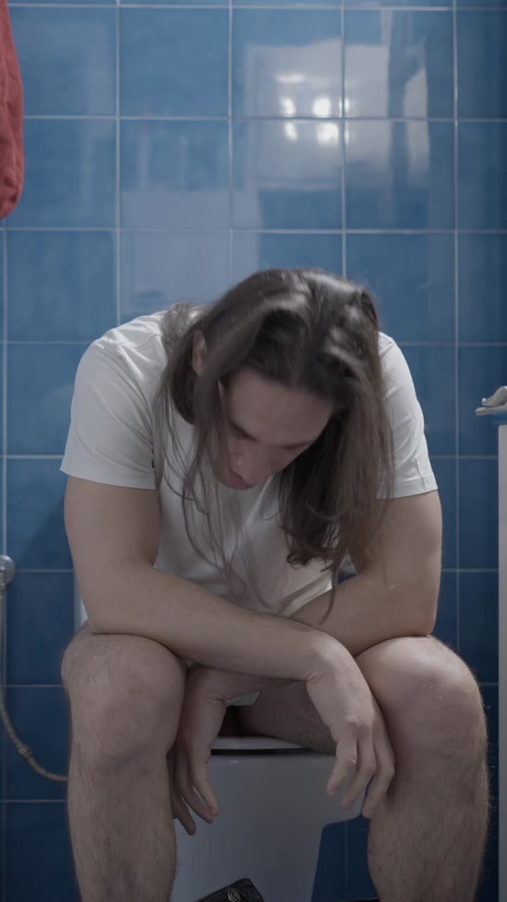 Man experiencing discomfort or pain while sitting on a toilet