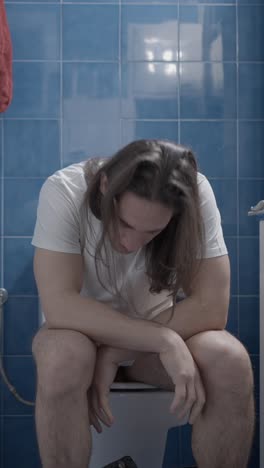 man experiencing discomfort or pain while sitting on a toilet
