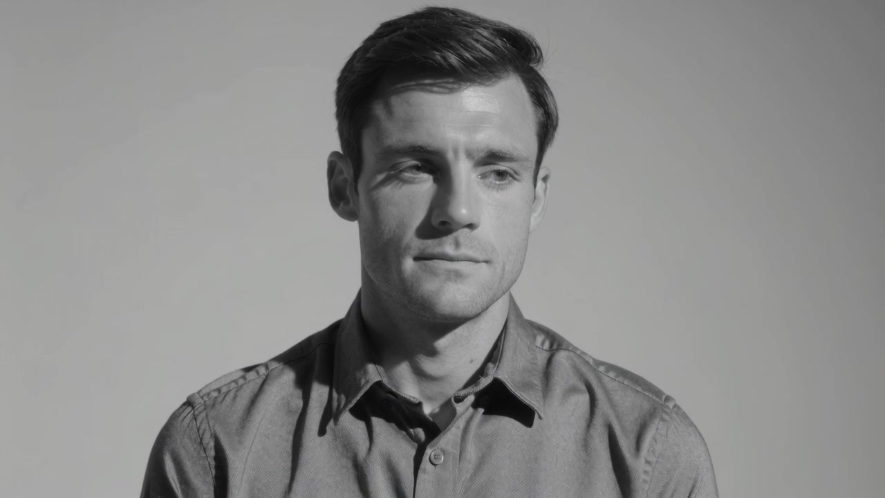 Starting adult male speaking, glancing to offframe cue in studio lighting, buttondown shirt