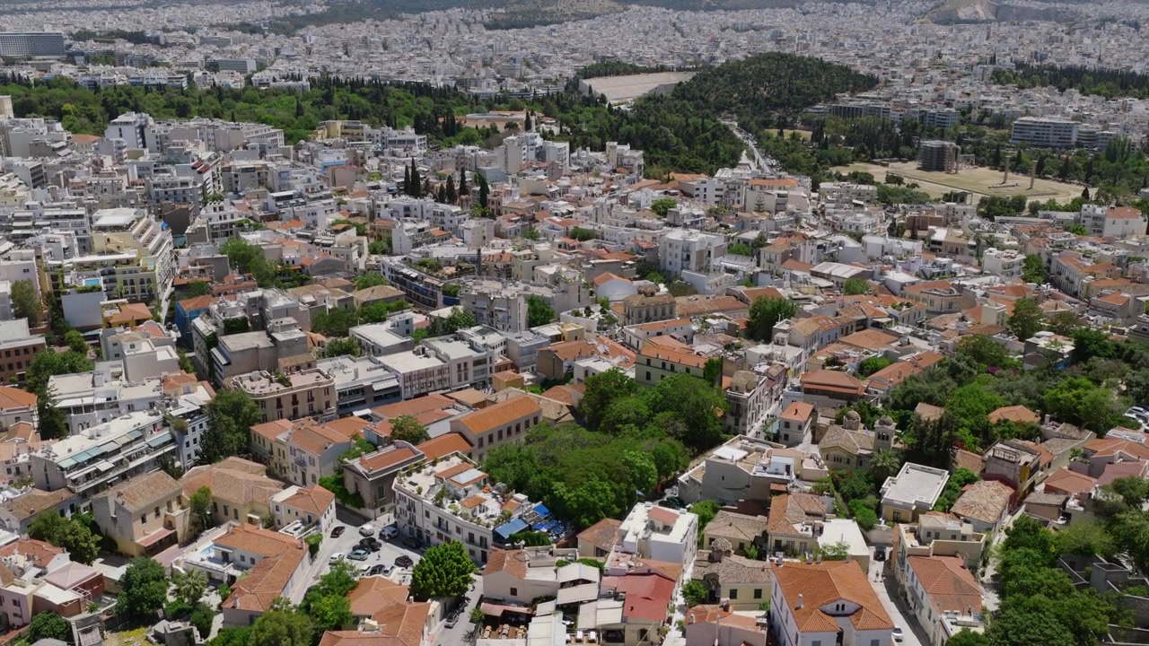 Veduta aerea di un quartiere di Atene vicino all'Acropoli, con tetti in terracotta, strade alberate e la città che si estende verso colline distanti