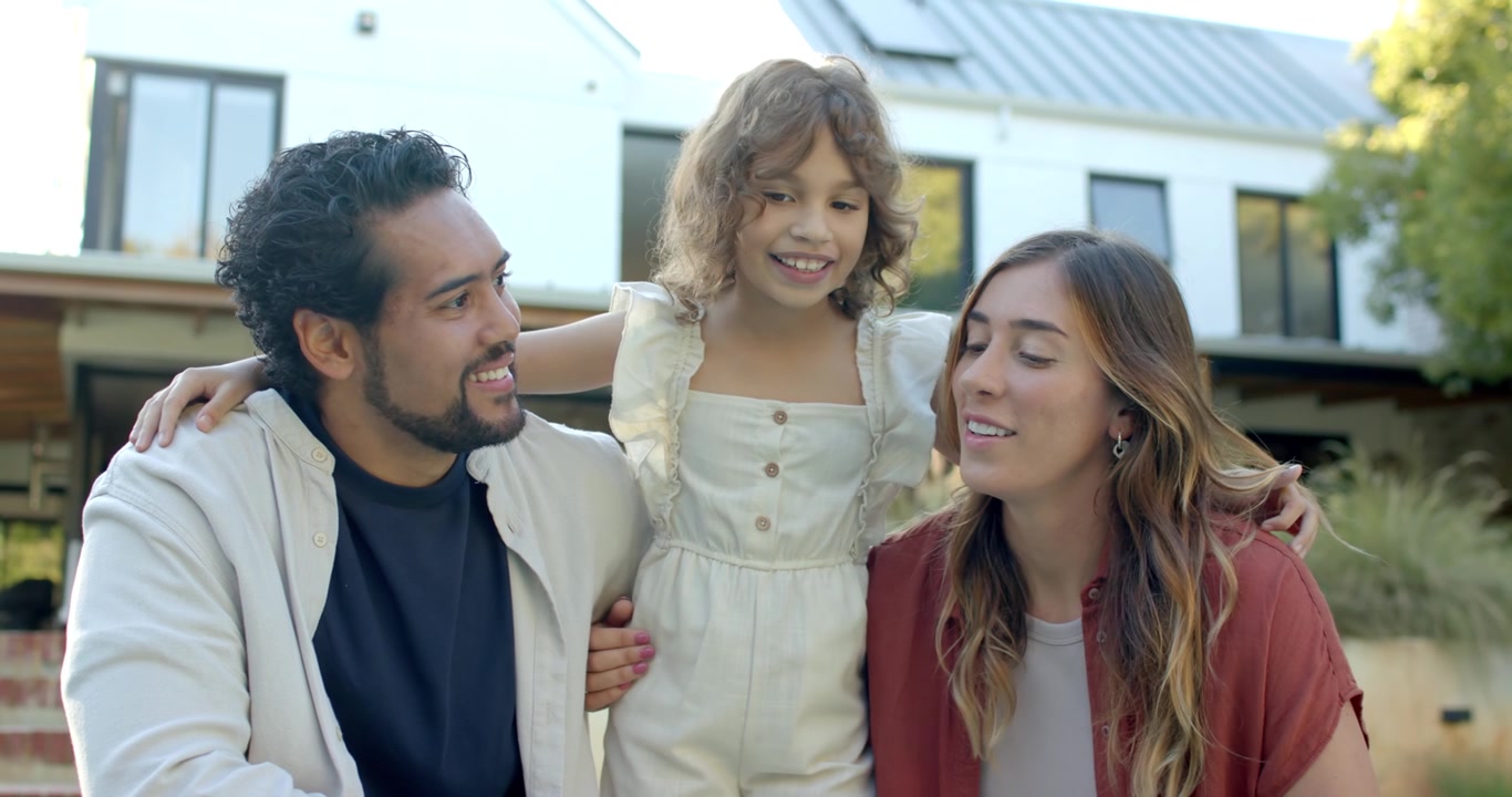Família ajoelhada com uma criança (menina) falando, pais virando-se sorrindo, criando laços na varanda, observando a pulseira.
