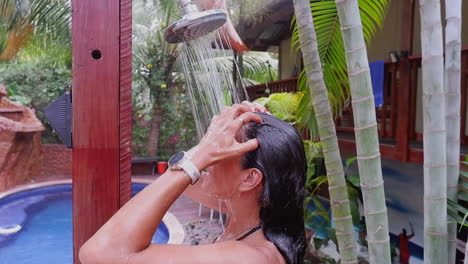 Woman-enjoys-post-swim-outdoor-shower-at-tropical-resort-swimming-pool