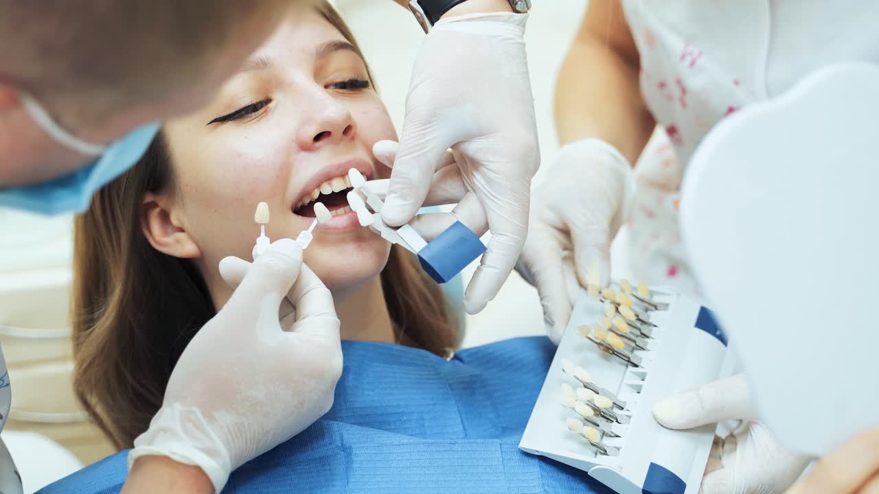 A dentist doctor in medical gloves with an assistant trying on dentures for a young girl. A palette of shades of teeth for dental prosthetics vitascale