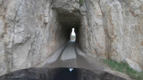 driving through a narrow rock tunnel on needles highway in custer state park, south dakota