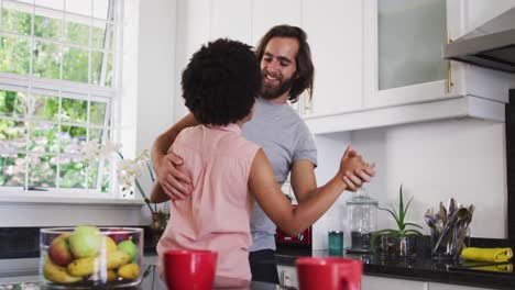 Mixed-race-couple-dancing-in-the-kitchen-at-home
