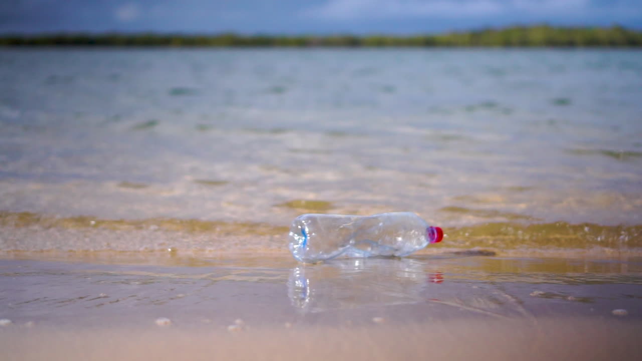 botella de plástico arrojada desde el exterior del marco en pequeñas olas que lamen en la playa de arena