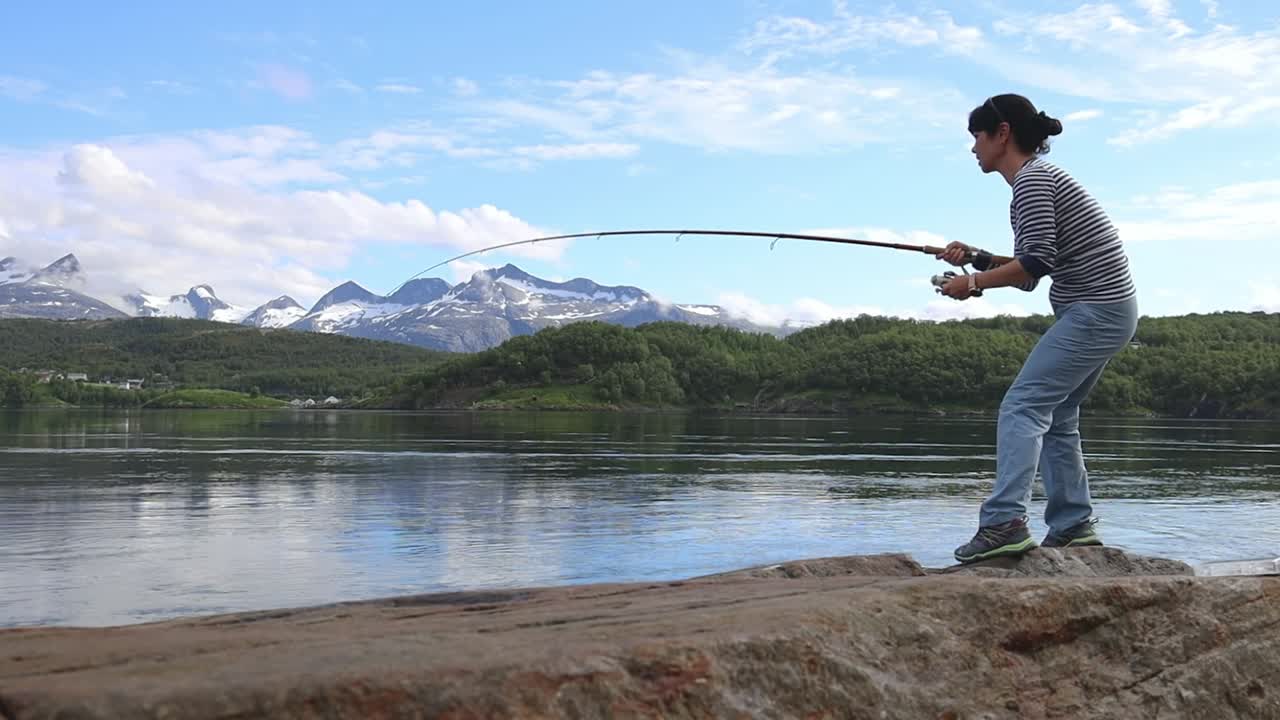 Seorang wanita menangkap ikan besar dengan joran pancing dan tidak bisa menariknya keluar dari air. Memancing dengan joran pancing di Norwegia. Memancing di Norwegia adalah cara untuk merangkul gaya hidup lokal.