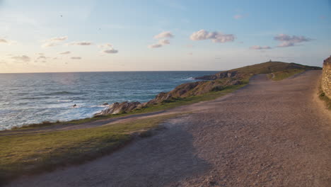 Coastal-Path-Next-to-Headland-Hotel-and-Spa-Holiday-Cottages-Overlooking-The-Sea-at-Golden-Hour,-Newquay,-Cornwall,-United-Kingdom---panning-shot