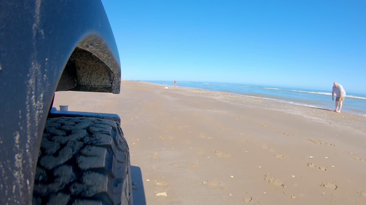 neumático delantero derecho del vehículo y gente caminando en las olas mientras conduce en una playa en un día soleado en la isla del padre sur, texas- punto de vista, punto de vista