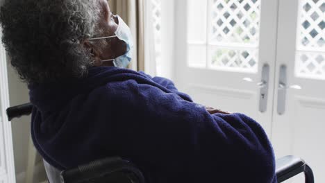 senior african american woman wearing face mask sitting on the wheelchair at home