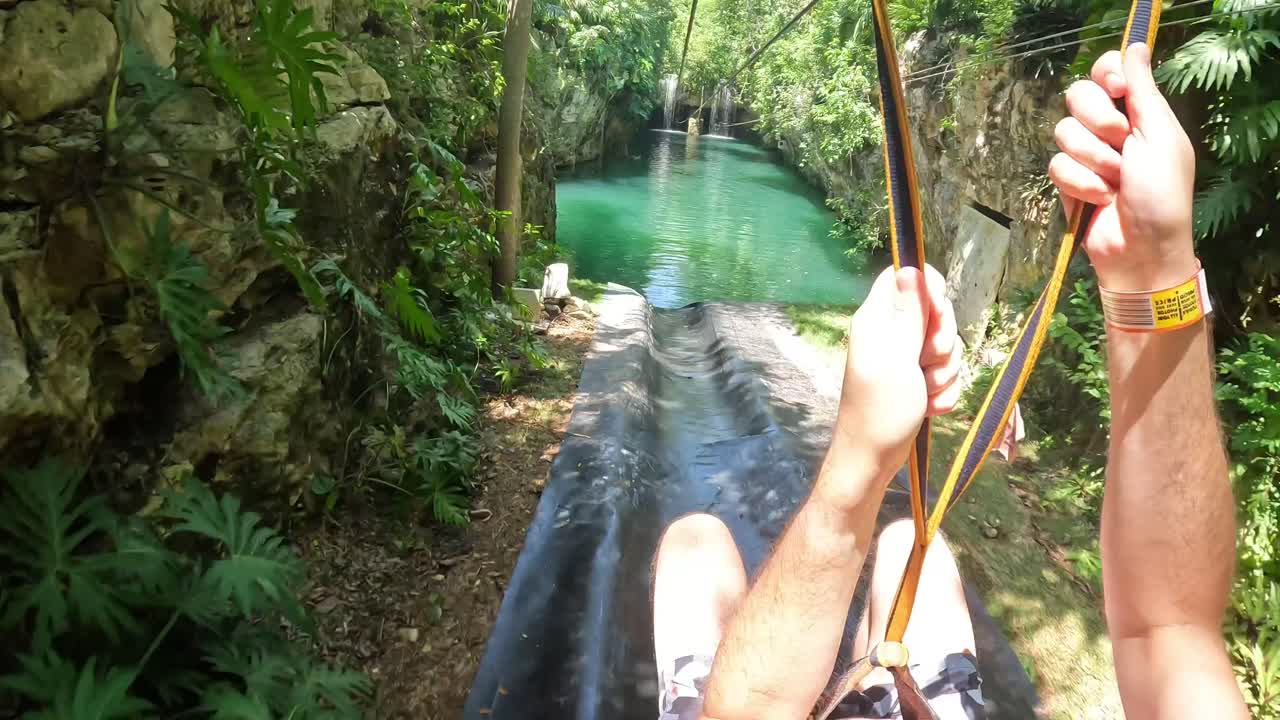 pov zip line pasando una cascada con un chapoteo aterrizando en un ambiente tropical