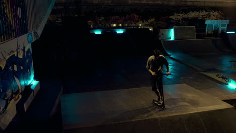 active teen riding scooter on ramp at night skate park. sportive man jumping.