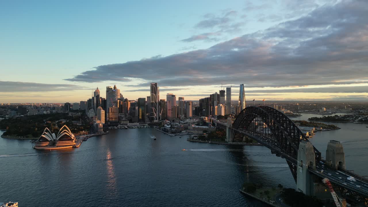 Il Sydney Harbour Bridge e la Sydney Opera House sul porto di Sydney durante un tramonto nuvoloso.