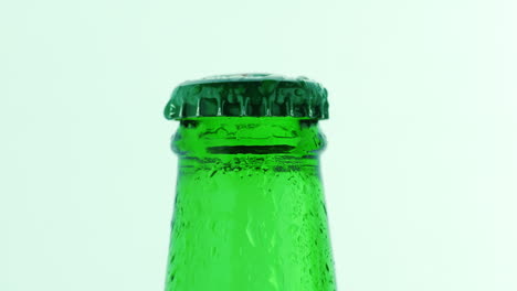 the neck of a green bottle with a cold drink covered with droplets of water slowly rotating on a whi