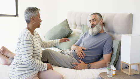 senior woman holding hands with man, sitting on bed in bedroom